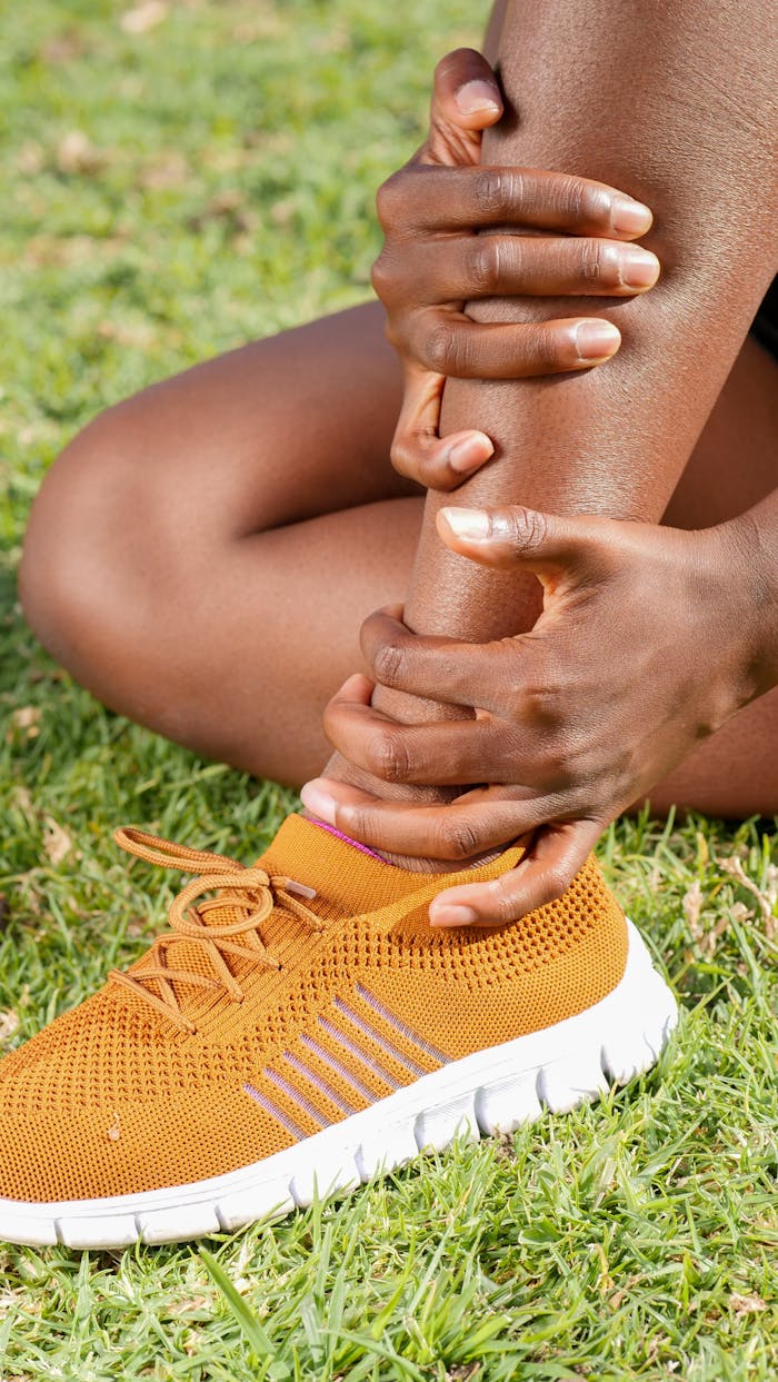 Close-up of a person holding their ankle, indicating injury or discomfort while sitting on grass.
